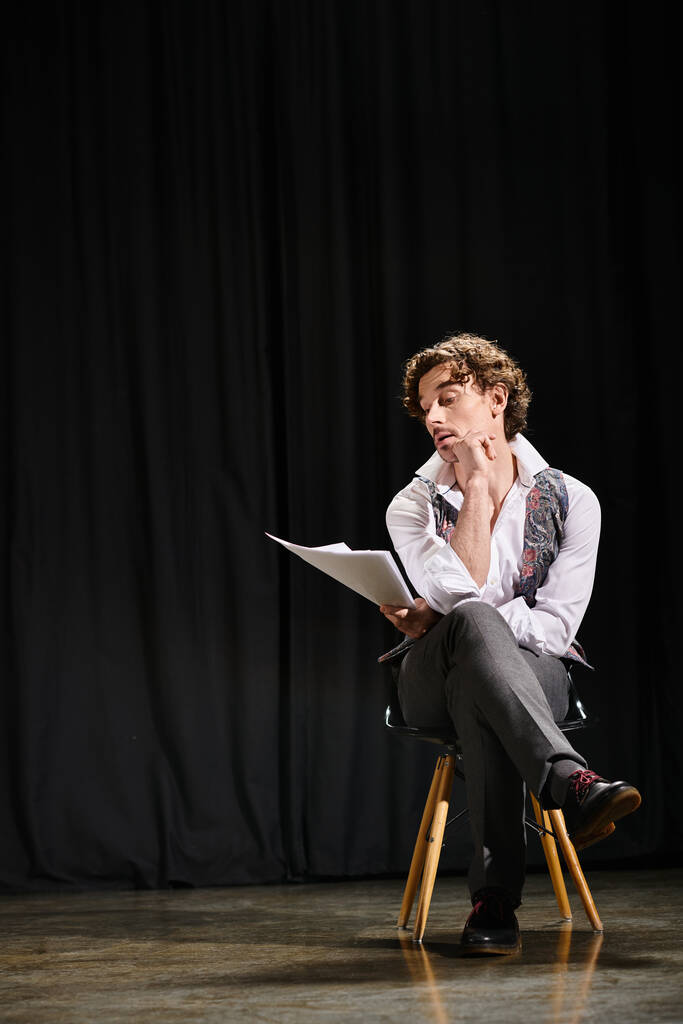 Ένας άντρας αφοσιωμένος στην ανάγνωση ενός σεναρίου ενώ καθόταν σε μια καρέκλα. - Φωτογραφία, εικόνα