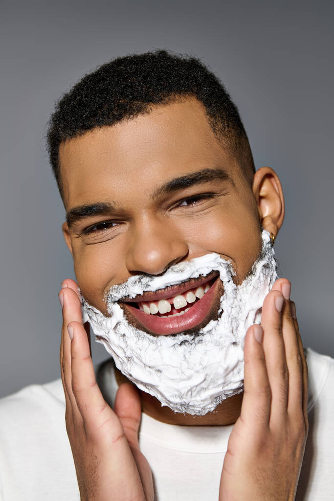 Αφροαμερικάνος χαρούμενος άντρας ξυρίζει το πρόσωπό του σαν μέρος μιας ρουτίνας περιποίησης του δέρματος.. - Φωτογραφία, εικόνα