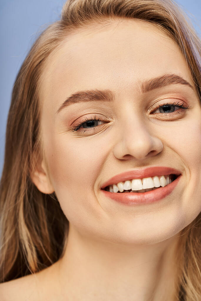 若い金髪の女性は,スタジオの設定で白い歯を見せながら喜んで微笑む. - 写真・画像