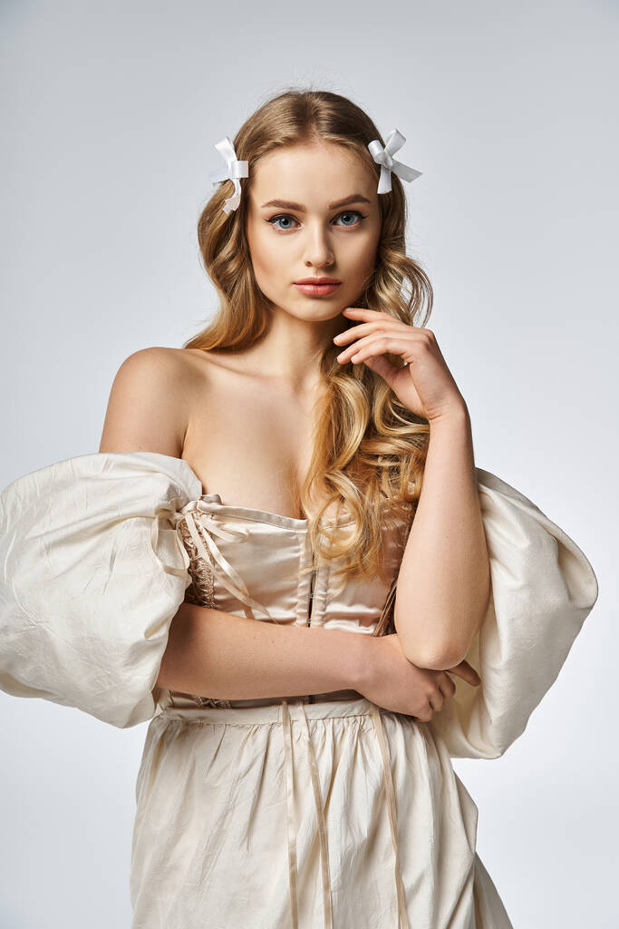 Egy fiatal, szőke nő fehér ruhában pózol egy elegáns stúdióban.. - Fotó, kép