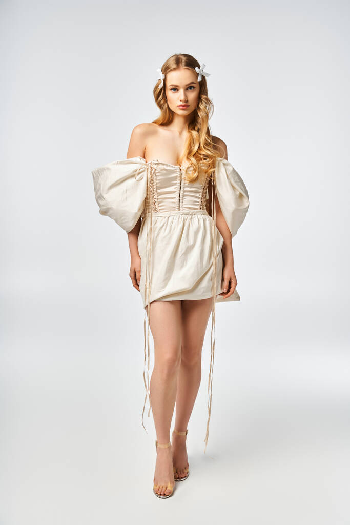 Eine junge blonde Frau steht elegant in einem weißen Kleid in einem Studio-Ambiente und strahlt Anmut und Charme aus. - Foto, Bild