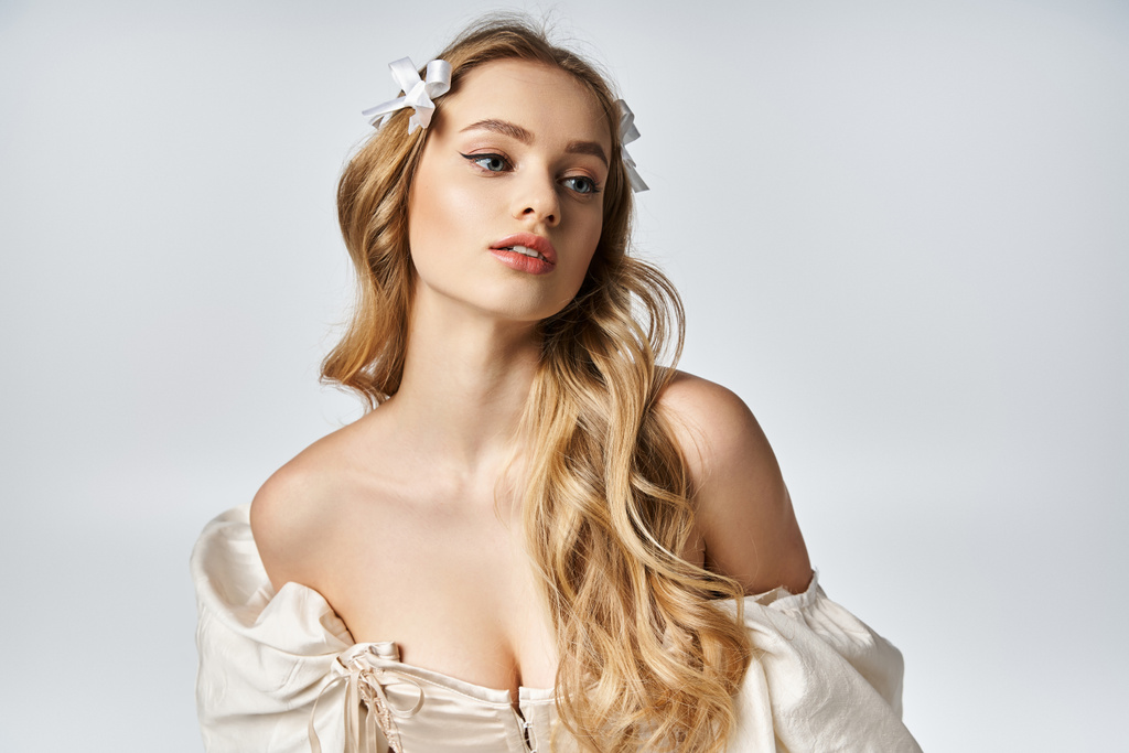 Eine junge, schöne blonde Frau posiert anmutig in einem fließenden weißen Kleid in einem Studio-Setting. - Foto, Bild