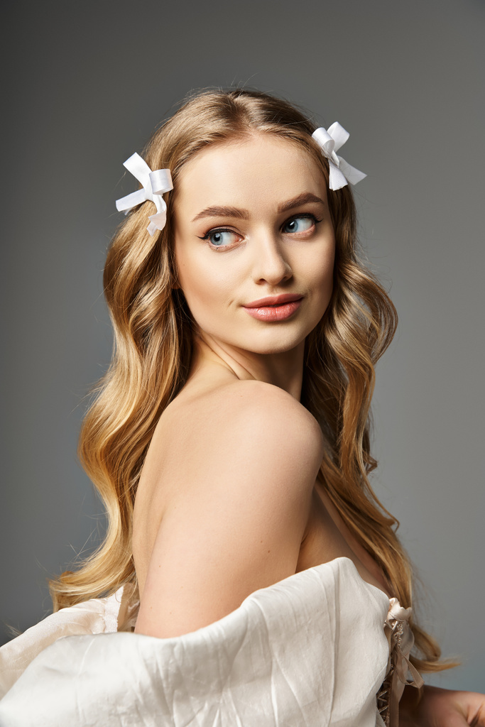 Młoda blondynka z długimi włosami elegancko pozuje w płynącej białej sukience w studio. - Zdjęcie, obraz