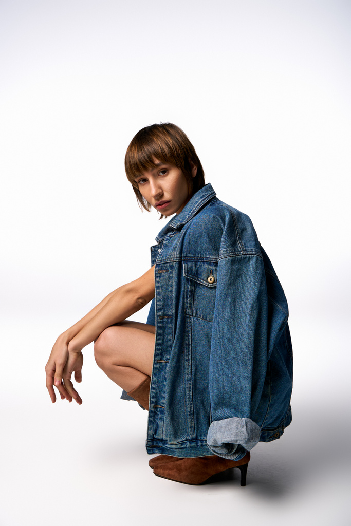 A young woman with a casual style sits on the ground in a jean jacket, exuding a relaxed and contemplative vibe. - Photo, Image
