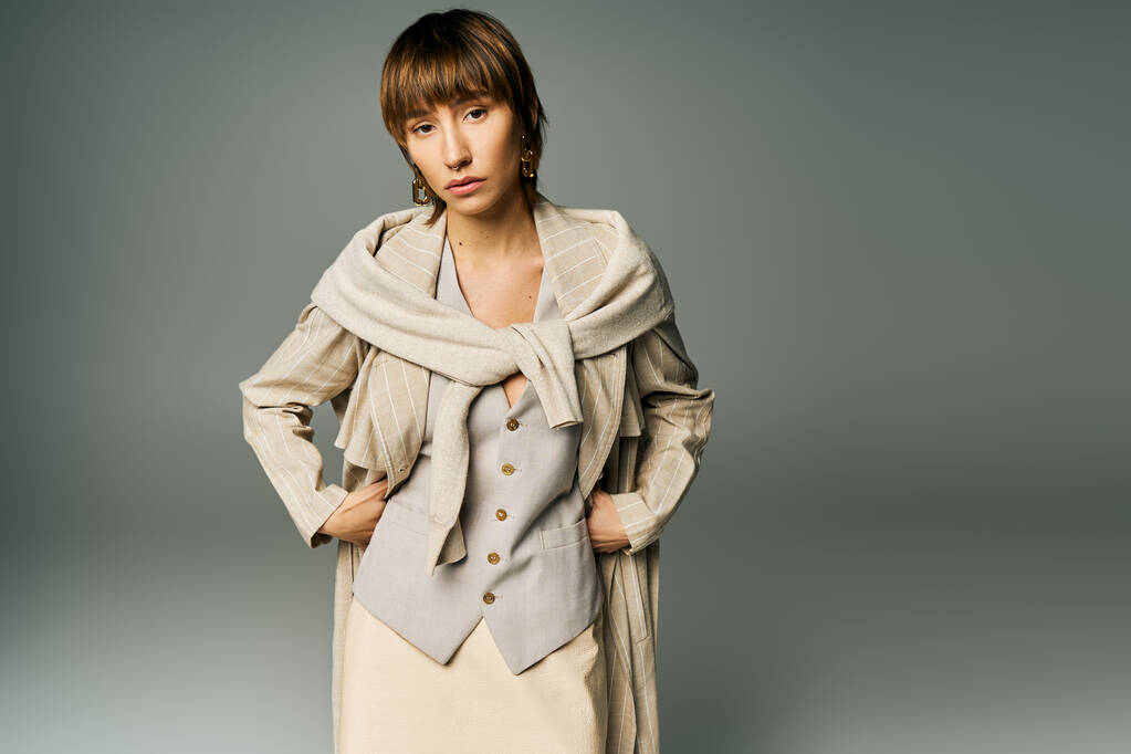 Egy rövid hajú, elegáns fiatal nő magabiztos pózt visel ruhában és dzsekiben egy stúdióban.. - Fotó, kép