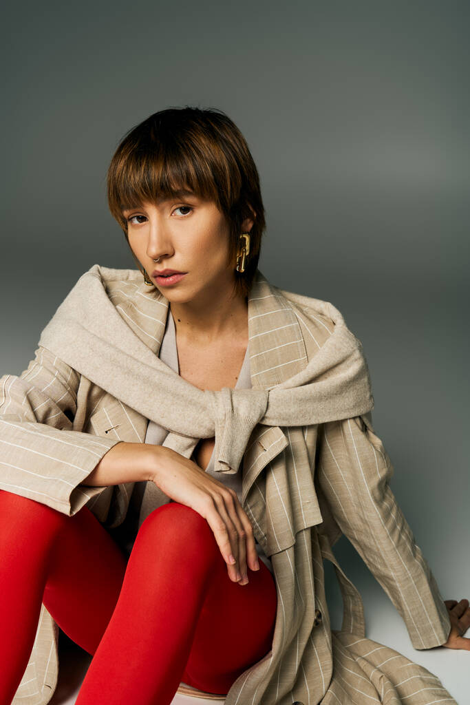 Mladá žena s krátkými vlasy sedí půvabně na podlaze ve studiu, na sobě zářivé červené punčocháče. - Fotografie, Obrázek