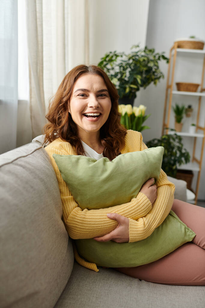 Kobieta w średnim wieku siedząca na kanapie, przytulająca miękką poduszkę. - Zdjęcie, obraz