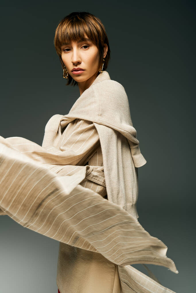 Eine junge Frau mit kurzen Haaren, in einem fließenden Kleid und einem Schal, verströmt Eleganz und Anmut in einem Studio-Setting. - Foto, Bild