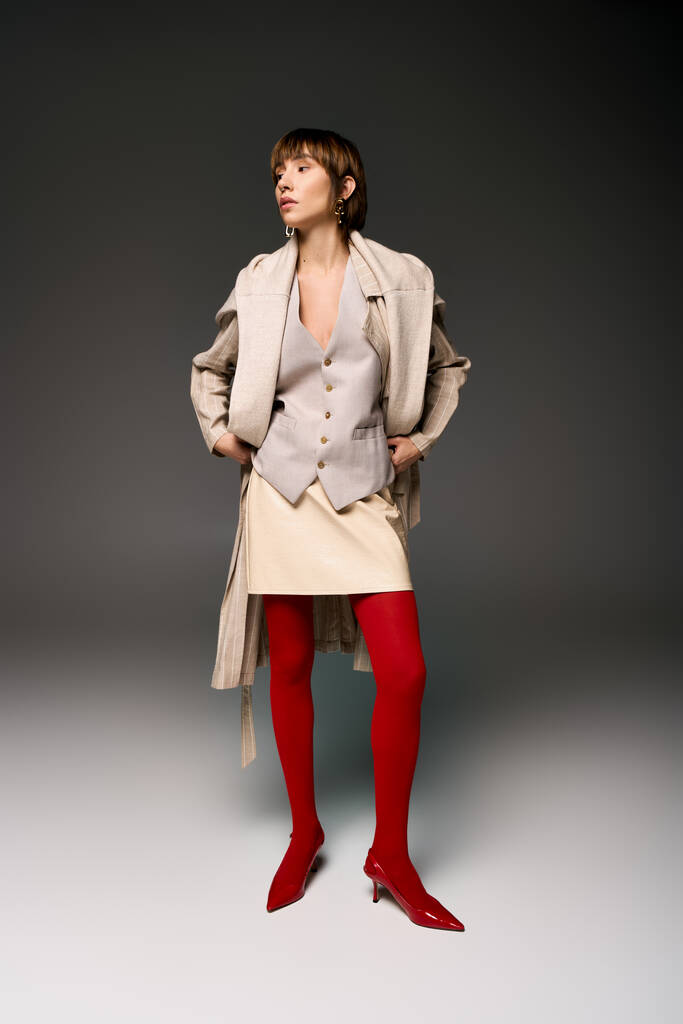 Een jonge vrouw met kort haar slaat een pose in panty en een jas in een studio setting. - Foto, afbeelding