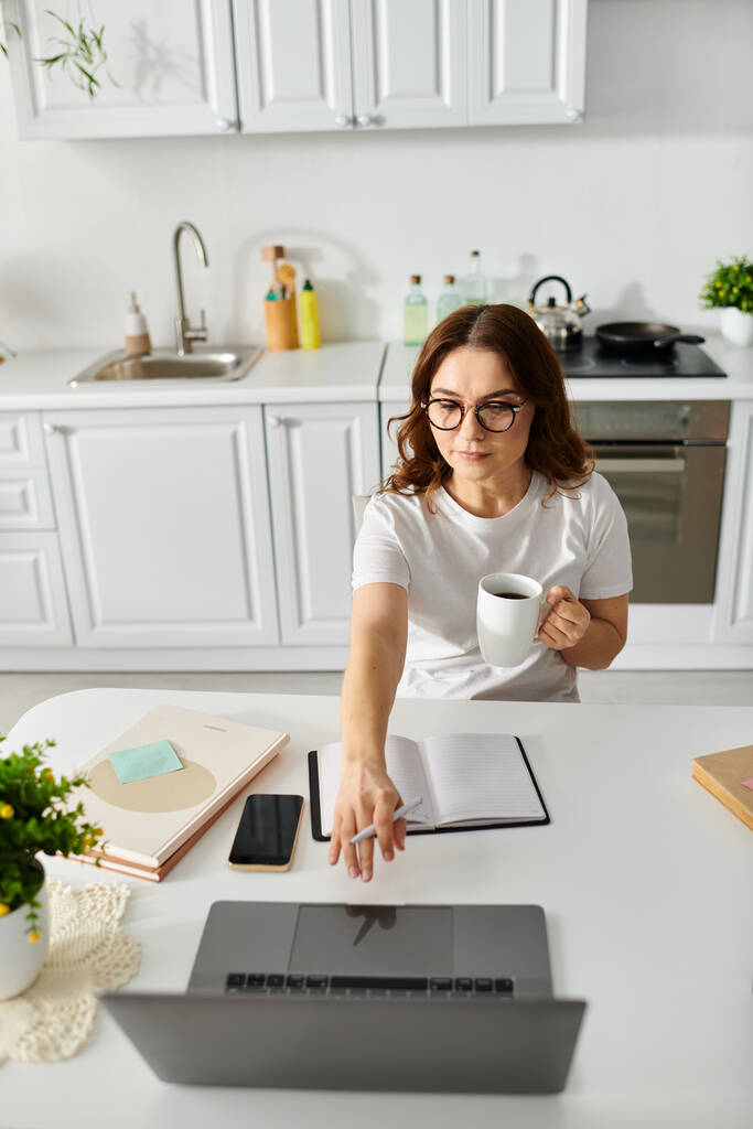 Žena středního věku pracuje na notebooku u kuchyňského stolu. - Fotografie, Obrázek