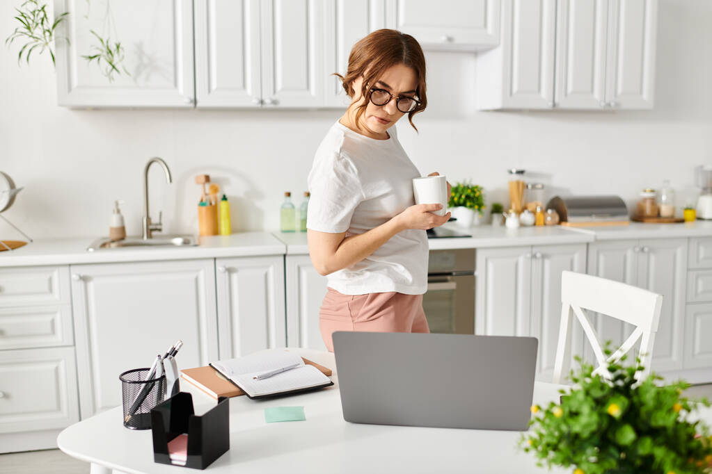 Женщина средних лет держит чашку кофе на уютной кухне. - Фото, изображение
