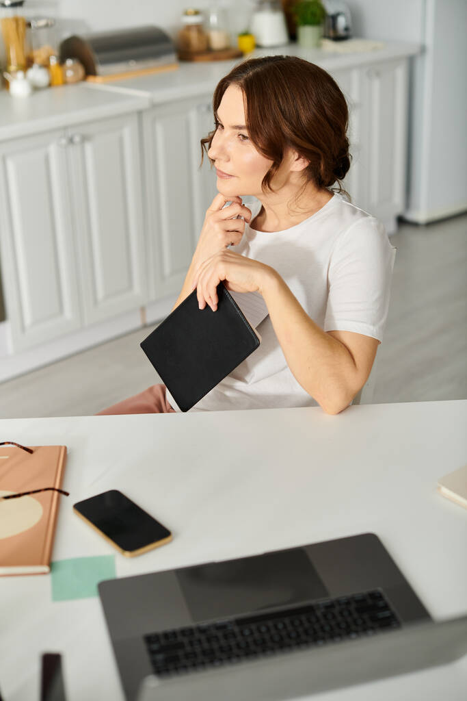 Žena středního věku sedící u kuchyňského stolu a používající tablet. - Fotografie, Obrázek