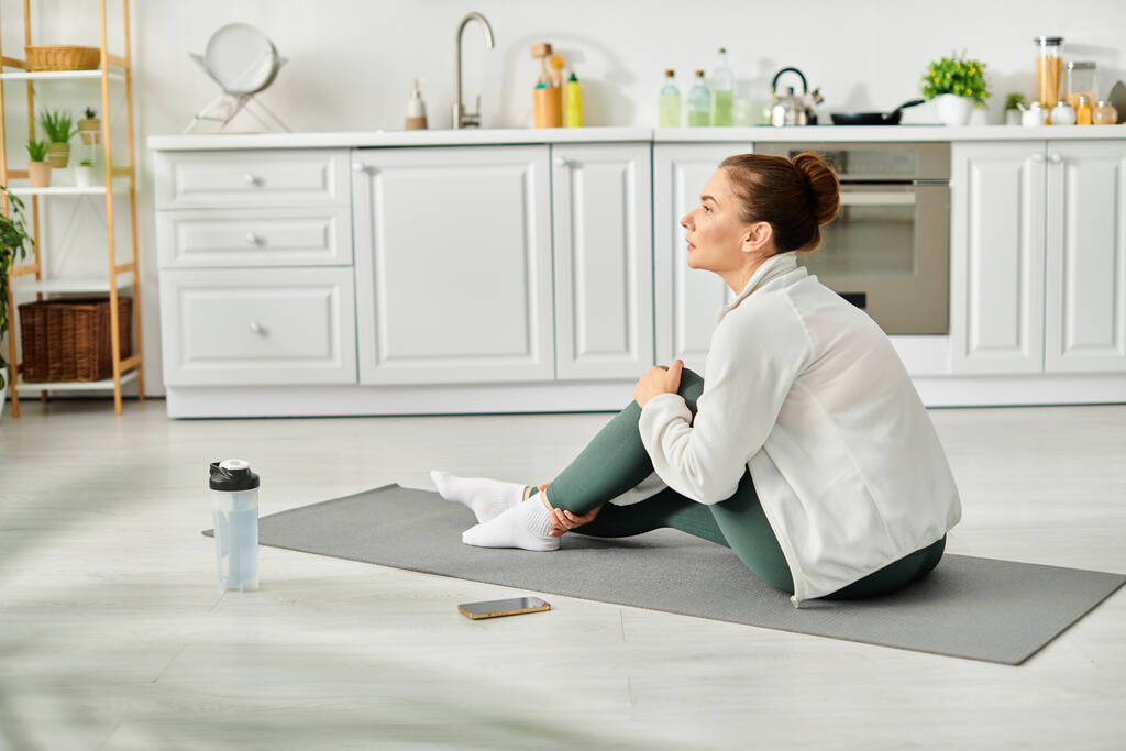 Donna di mezza età pratica pacificamente yoga sul suo tappeto in una cucina accogliente. - Foto, immagini
