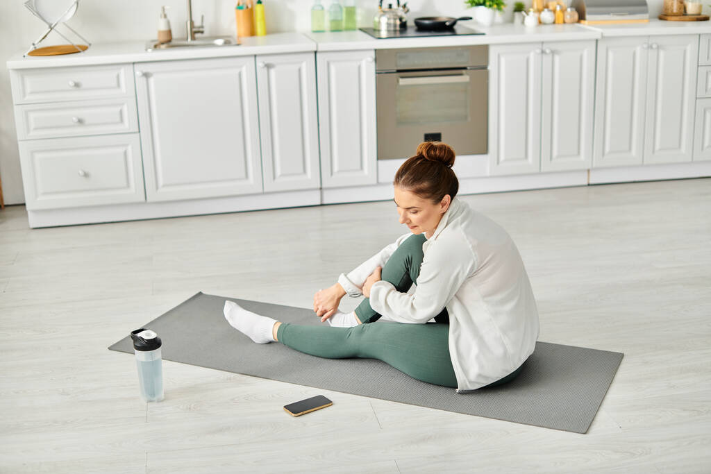 Жінка середнього віку знаходить внутрішній спокій на килимку для йоги на своїй кухні. - Фото, зображення