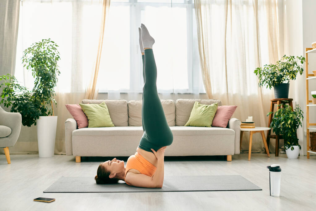 Middle-aged woman performing a handstand in her living room. - Photo, Image