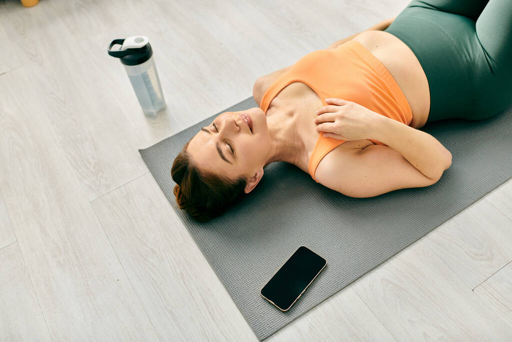 Frau mittleren Alters liegt auf Yogamatte und benutzt Handy. - Foto, Bild