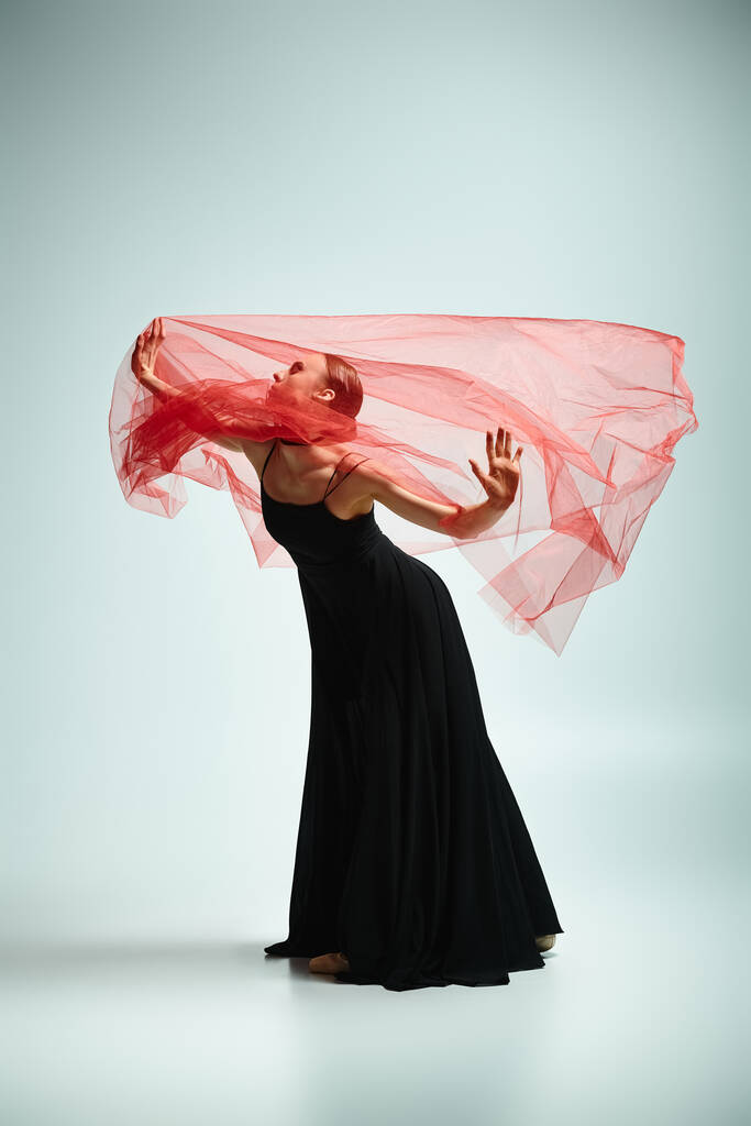 Uma bailarina bonita nova em um vestido preto fluindo e danças vermelhas vibrantes do cachecol graciosamente. - Foto, Imagem