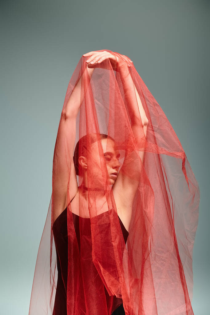 Una joven bailarina baila con gracia con un vibrante velo rojo en la cabeza. - Foto, Imagen