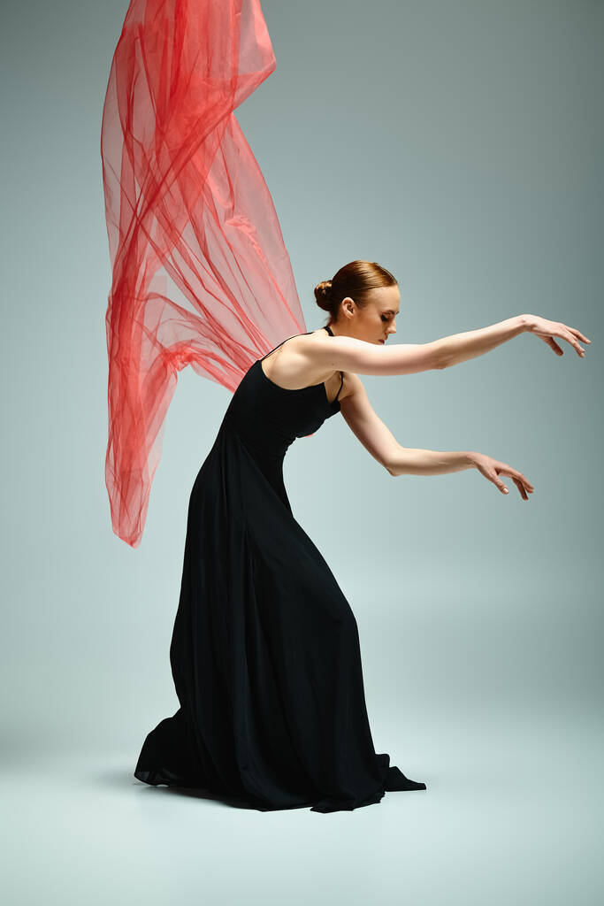 Mladá, krásná baletka v černých šatech se elegantně pohybuje s červeným závojem. - Fotografie, Obrázek