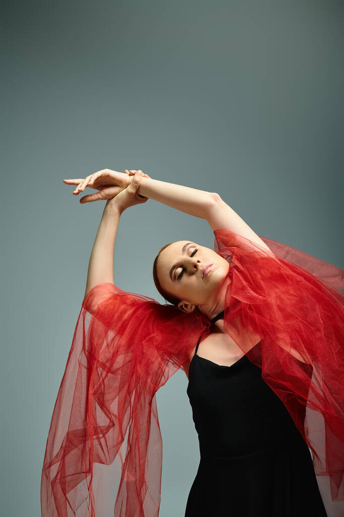 Μια νεαρή μπαλαρίνα με μαύρο φόρεμα και κόκκινο πέπλο χορεύει με χάρη. - Φωτογραφία, εικόνα