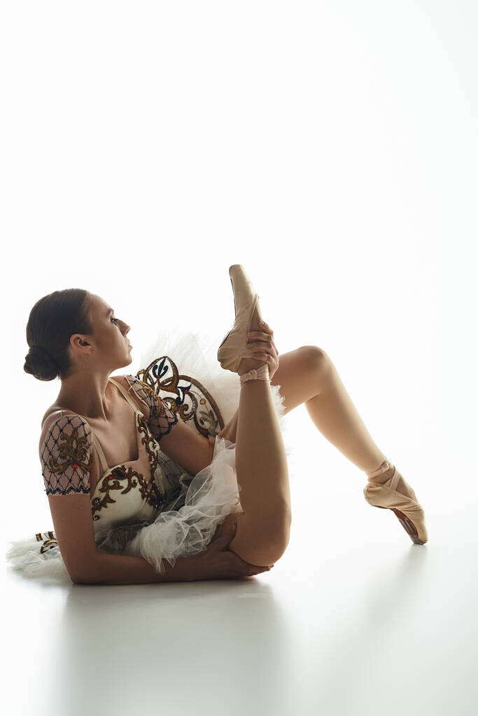 Eine junge Ballerina liegt anmutig auf dem Boden, mit überkreuzten Beinen. - Foto, Bild