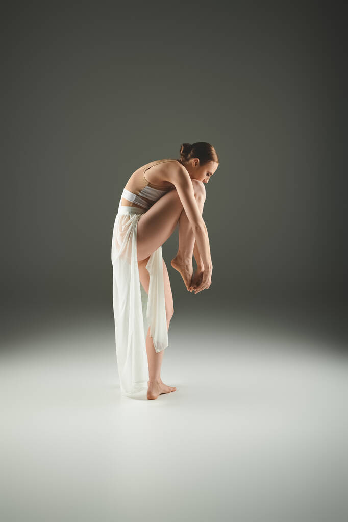 Una joven y hermosa bailarina con un vestido blanco se inclina elegantemente. - Foto, Imagen