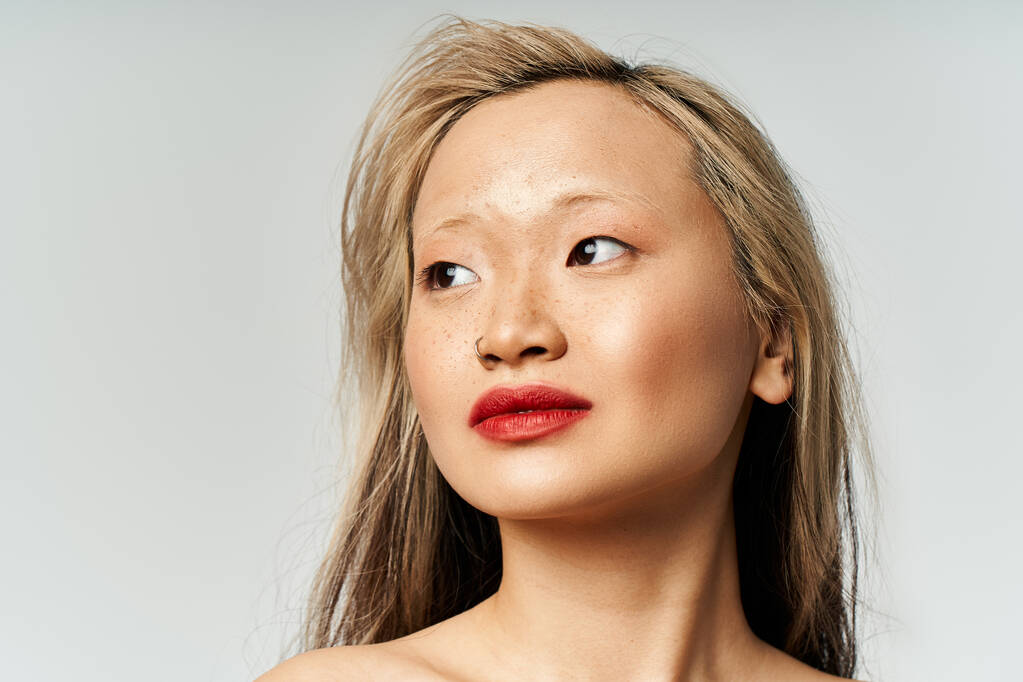 Una atractiva mujer asiática con el pelo largo y lápiz labial rojo posa con confianza en un atuendo vibrante. - Foto, Imagen