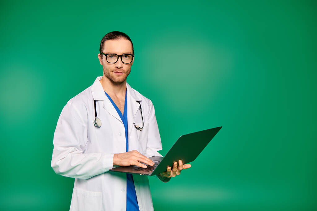 Красивый врач в халате уверенно держит ноутбук на зеленом фоне.. - Фото, изображение