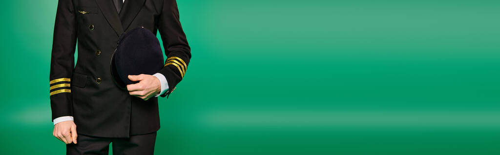Jóképű pilóta fekete öltönyben és nyakkendőben pózol élénk zöld háttér előtt. - Fotó, kép