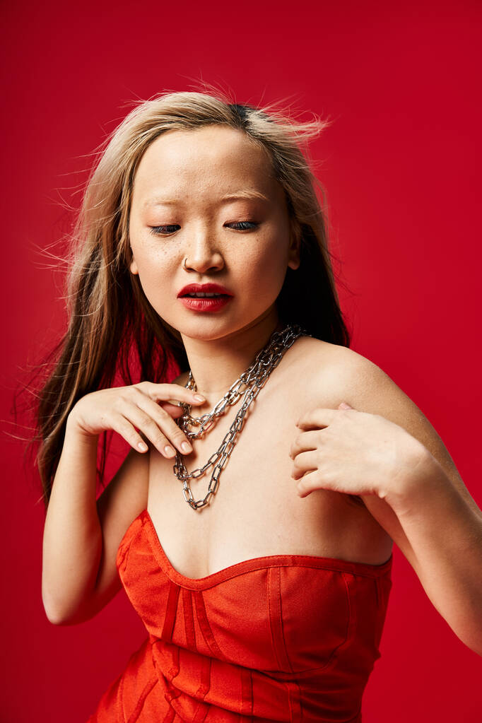 Uma mulher asiática cativante em um vestido vermelho vibrante bate uma pose graciosa para uma foto. - Foto, Imagem