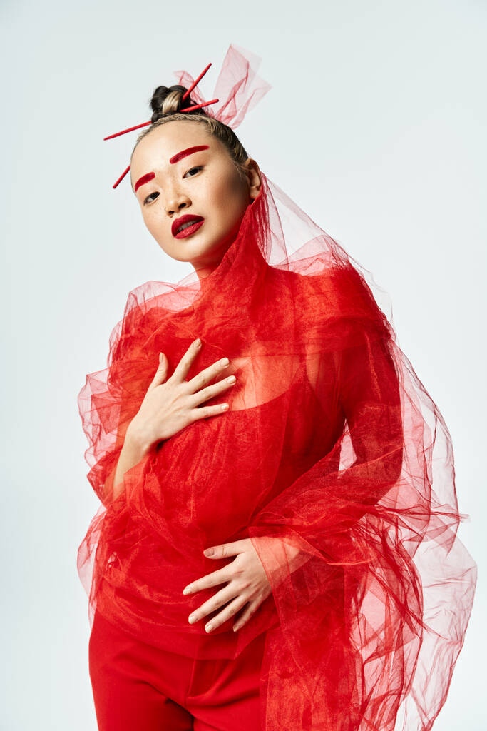Una atractiva asiática vestida de rojo vibrante baila graciosamente con un velo en la cabeza. - Foto, imagen