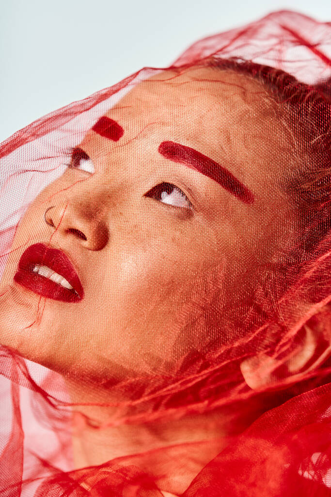 Een Aziatische vrouw versierd met levendige rode make-up en een sluier stelt actief. - Foto, afbeelding