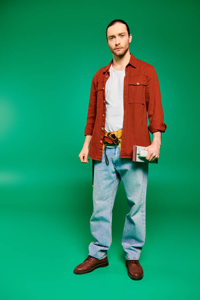 Ein gut aussehender männlicher Arbeiter in Uniform mit Werkzeug posiert vor grünem Hintergrund. - Foto, Bild