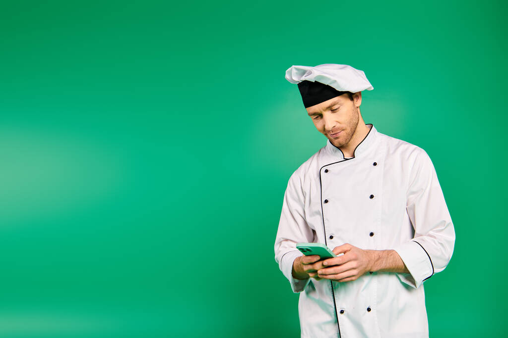 Ein männlicher Koch in weißer Uniform hält ein Handy in der Hand. - Foto, Bild