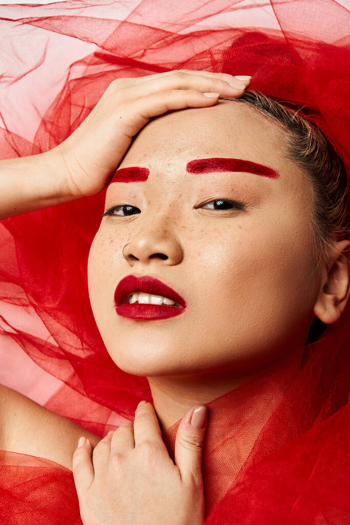 Une femme asiatique ornée de maquillage rouge et d'un voile rouge pose dynamiquement. - Photo, image
