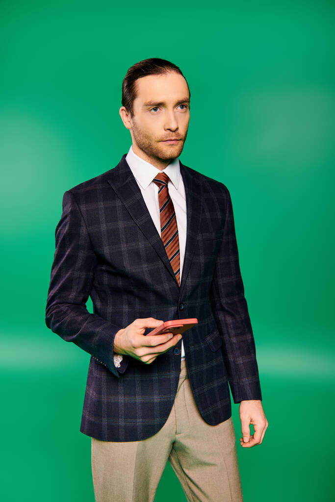 Bello uomo d'affari in abito chic e cravatta utilizzando il telefono cellulare su sfondo verde. - Foto, immagini