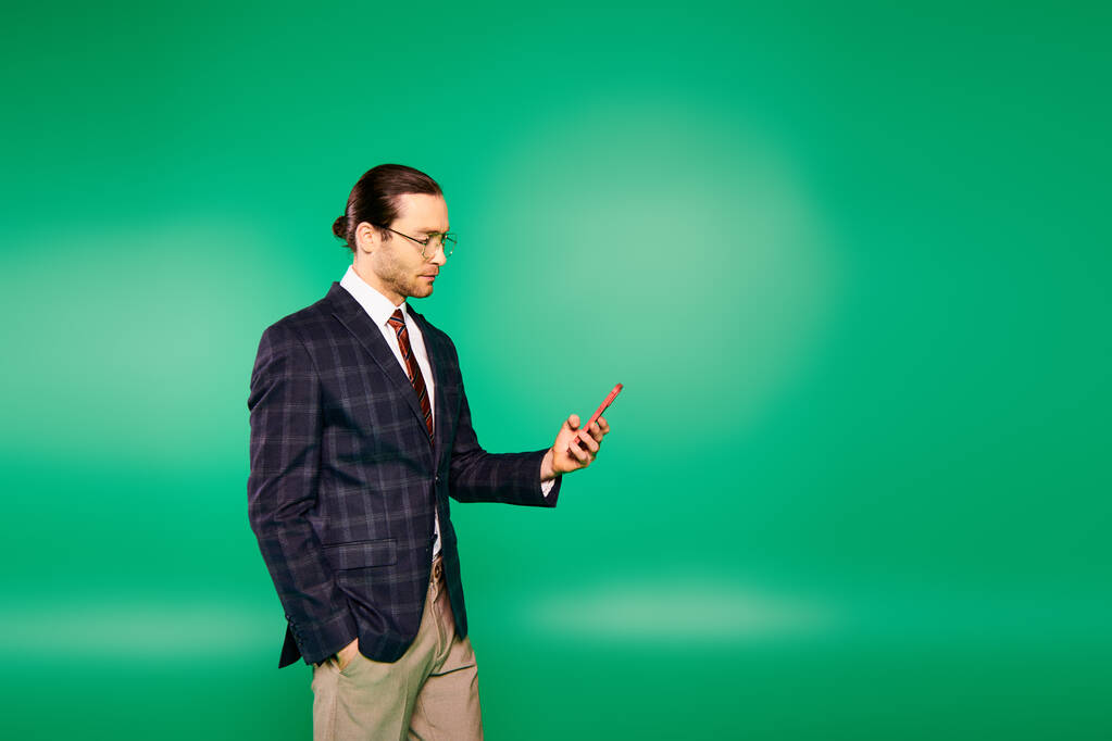 Egy jóképű üzletember elegáns öltönyben, aki mobilt tart a zöld vászon előtt.. - Fotó, kép