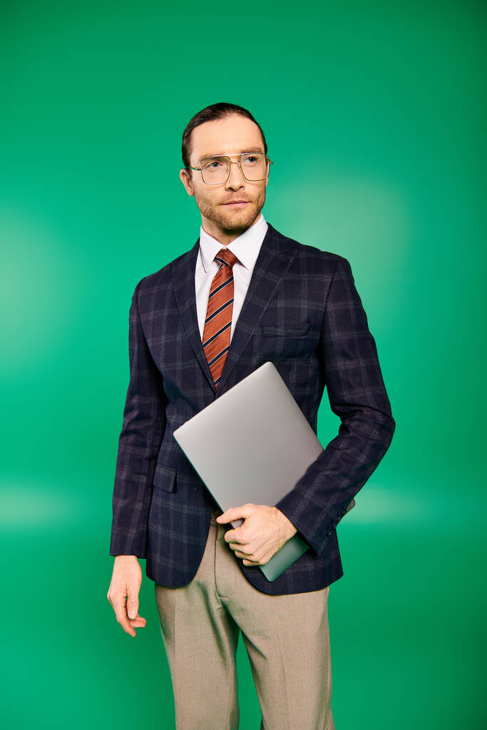 Elegáns üzletember elegáns öltönyben és nyakkendőben, kezében egy laptop zöld háttérrel. - Fotó, kép