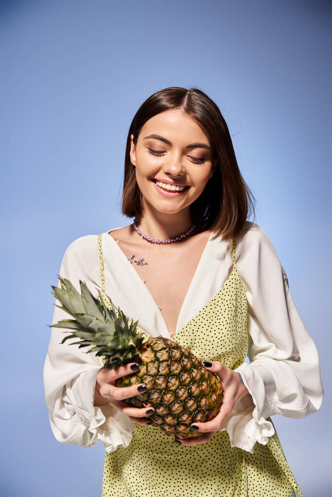 Egy barna hajú fiatal nő boldogan tart egy friss ananászt egy fényes stúdióban.. - Fotó, kép