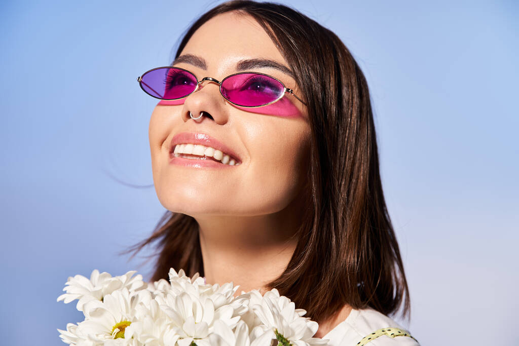 Stylowa brunetka w okularach przeciwsłonecznych posiada żywy bukiet kwiatów, emanujący poczuciem piękna i radości. - Zdjęcie, obraz