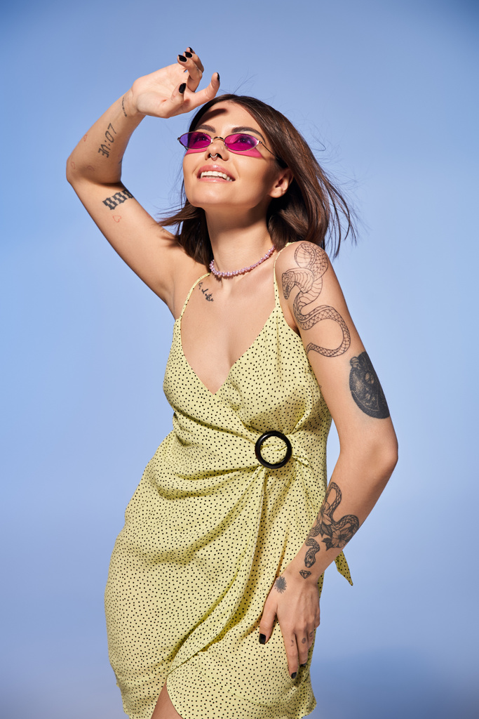 Brunette nainen upea keltainen mekko ylpeänä osoittaa pois hänen monimutkainen käsivarsi tatuoinnit studio ympäristössä. - Valokuva, kuva