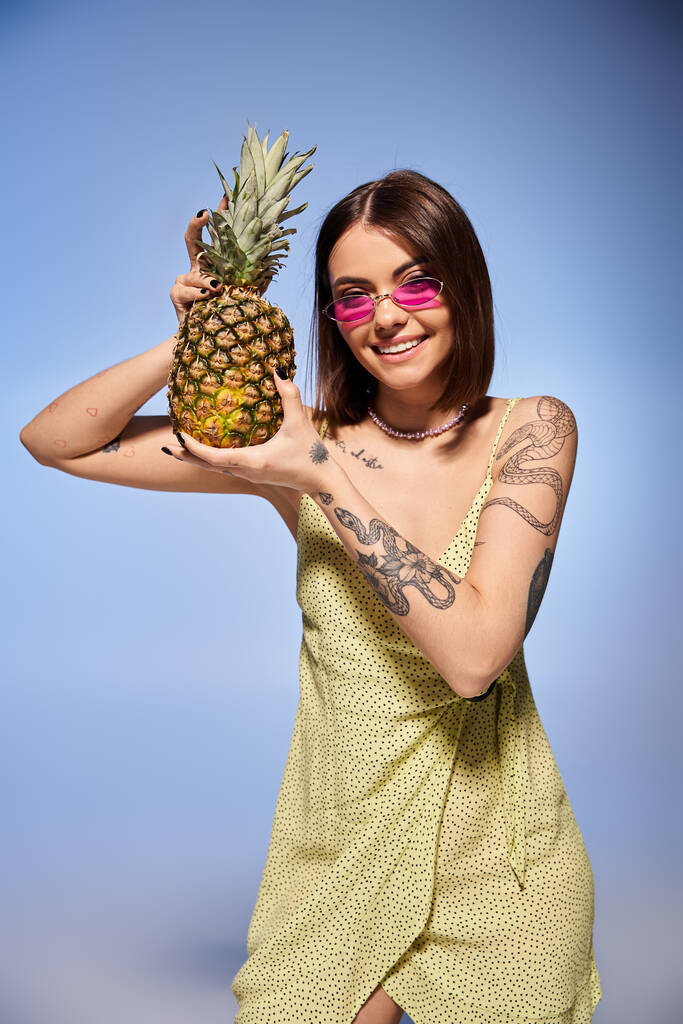 Młoda kobieta z brunetką pozuje w studio w jasnożółtej sukience, trzymając żywy ananas. - Zdjęcie, obraz