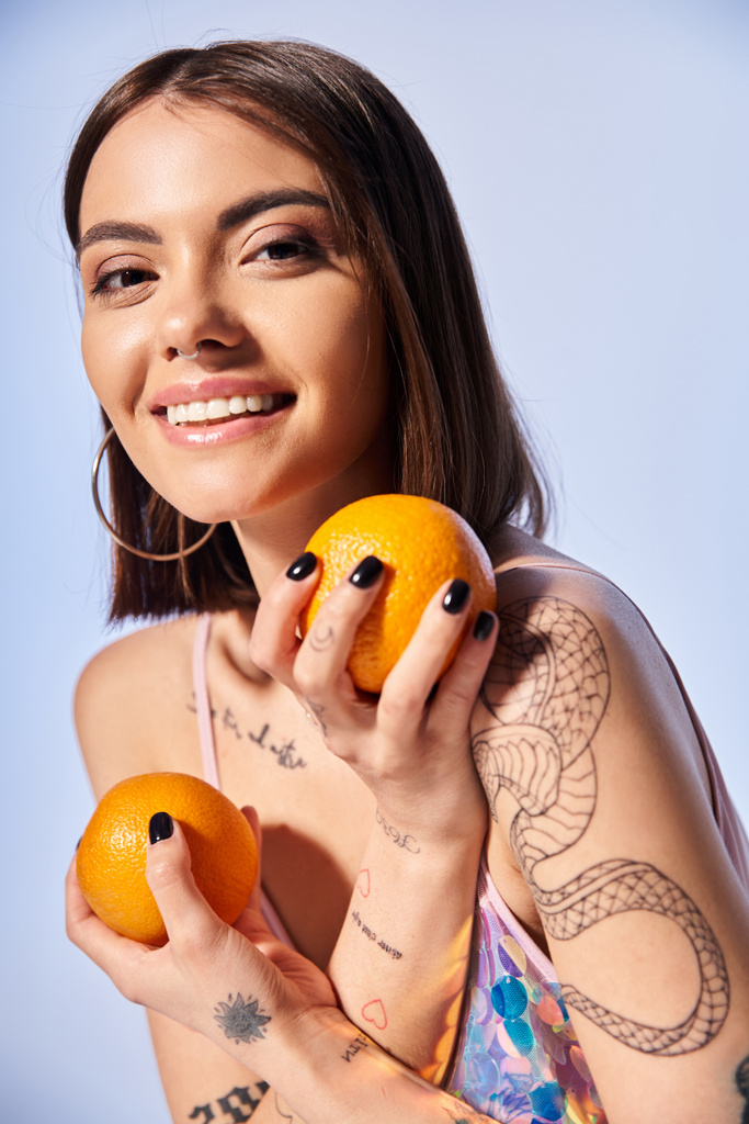 Młoda kobieta z włosami brunetki delikatnie trzyma w dłoniach dwa pomarańcze, pokazując ich żywy kolor i teksturę. - Zdjęcie, obraz