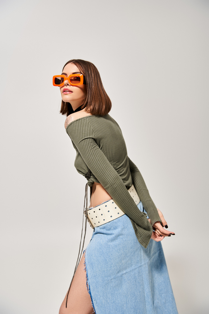 Eine stylische brünette Frau mit Rock und Sonnenbrille strahlt in einem Studioambiente Zuversicht aus. - Foto, Bild