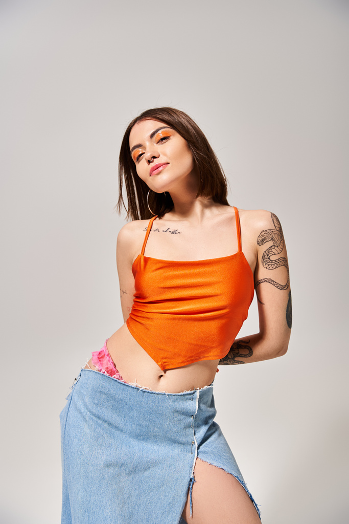 A stylish young woman with brunette hair poses in a studio wearing an orange top and a flowing blue skirt. - Photo, Image
