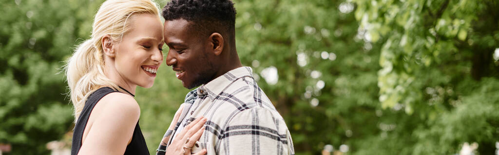 Um casal multicultural, um homem afro-americano e uma mulher caucasiana, de pé lado a lado ao ar livre em um parque. - Foto, Imagem