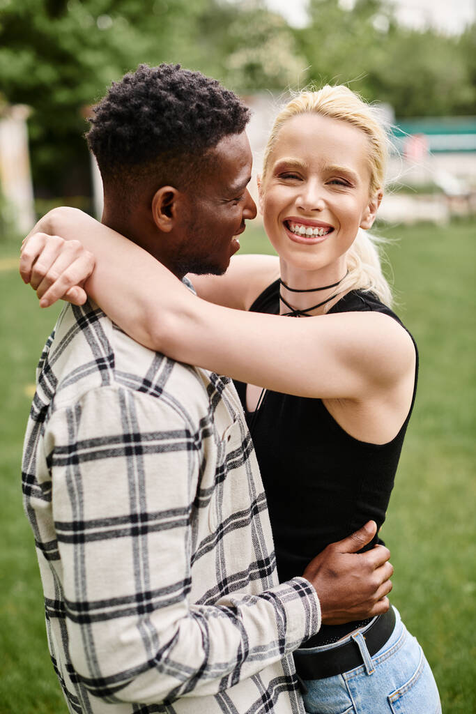 Ein glückliches Paar, bestehend aus einem afroamerikanischen Mann und einer kaukasischen Frau, das sich inmitten eines lebhaften Parks liebevoll umarmt. - Foto, Bild