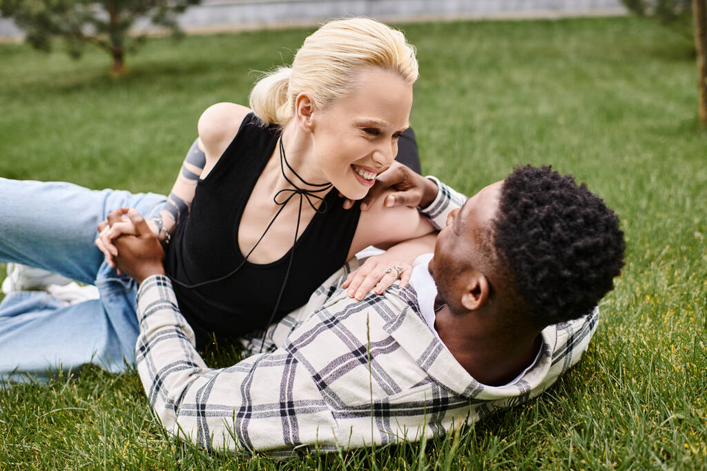 Un couple multiculturel heureux, un homme afro-américain et une femme caucasienne, se détendre ensemble dans l'herbe verte luxuriante d'un parc. - Photo, image