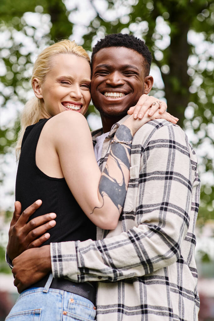 Una pareja feliz y multicultural, un hombre negro y una mujer caucásica, se abrazan amorosamente en un entorno de parque. - Foto, imagen
