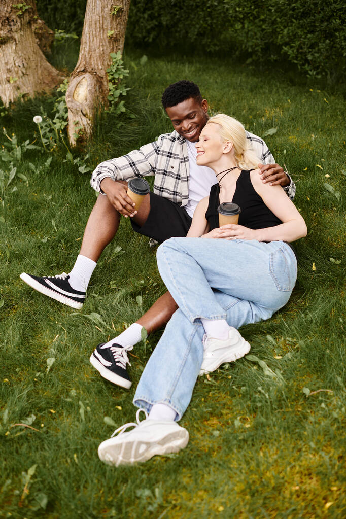 Un contenuto uomo afroamericano e donna caucasica siedono insieme su una lussureggiante erba verde, godendo di un momento di pace all'aperto. - Foto, immagini